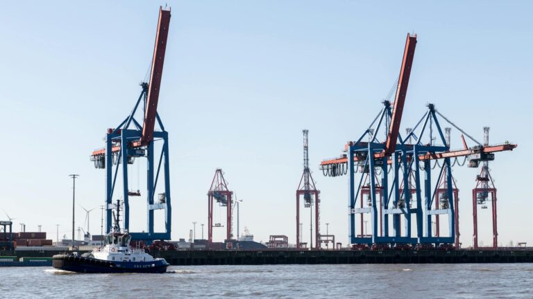A scenic view of Hamburg's bustling port featuring large cranes and a passing tugboat.
